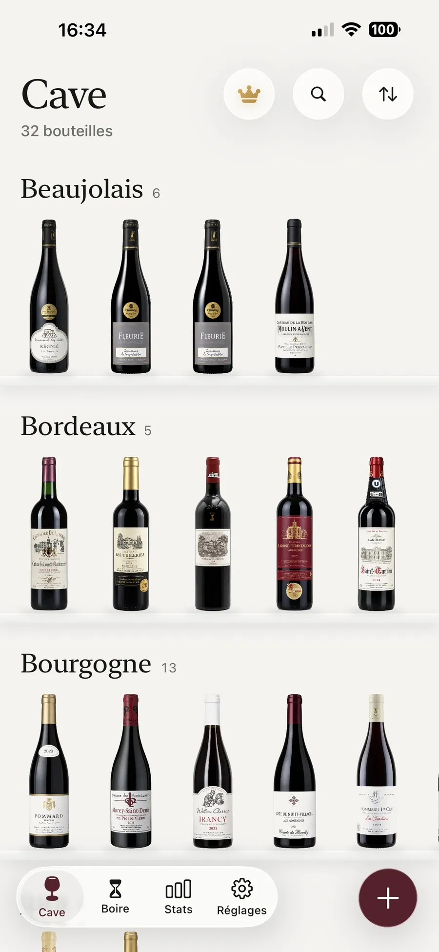 La cave de Kav rangée en étagère, avec une rangée de Beaujolais, une de Bordeaux et une de Bourgogne, les bouteilles posées sur des tablettes de verre